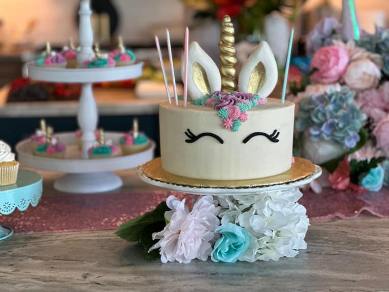 A unicorn-themed celebration cake and cupcake display on a dessert table