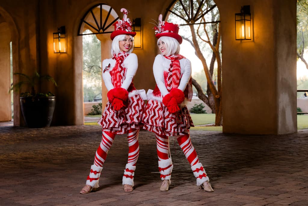 Two peppermint-striped performers pose together under an archway