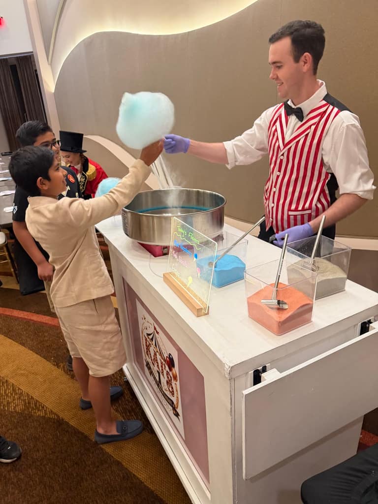 A striped-vest attendant spins fresh cotton candy at a circus-style confection cart